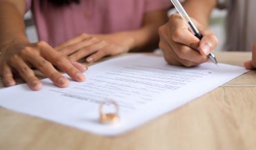 Husband Writing Signature on Marriage Paperwork After Agreement at Family Law Office.