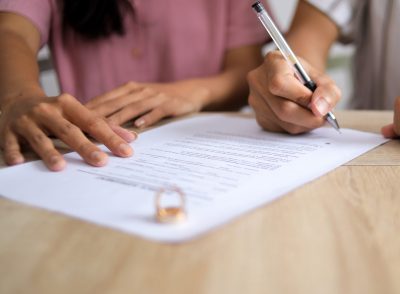 Husband Writing Signature on Marriage Paperwork After Agreement at Family Law Office.